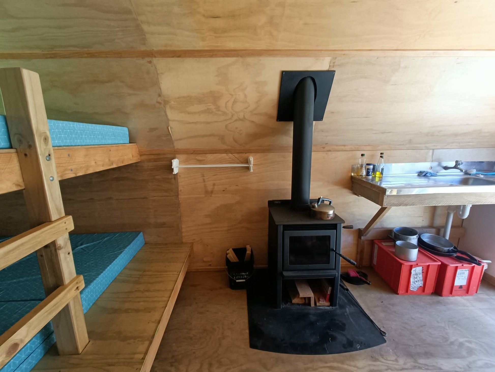Wooden interior of a cabin with a stove and bunk beds.